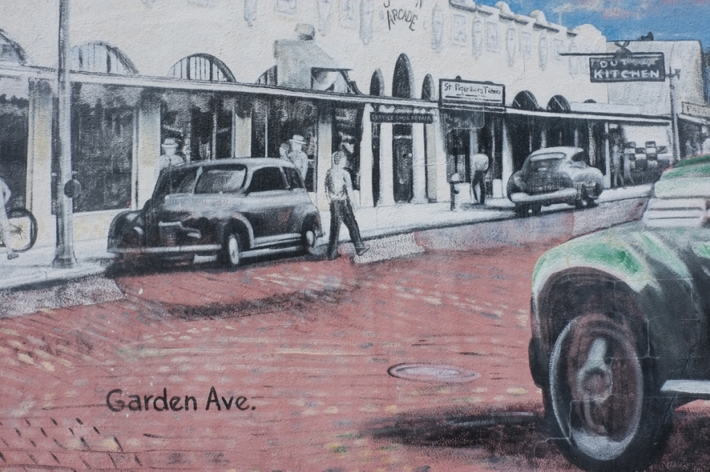 part of mural showing history of clearwater, Garden Avenue, old cars, brick streets, some pedestrians, a row of stores, inclusing a restaurant