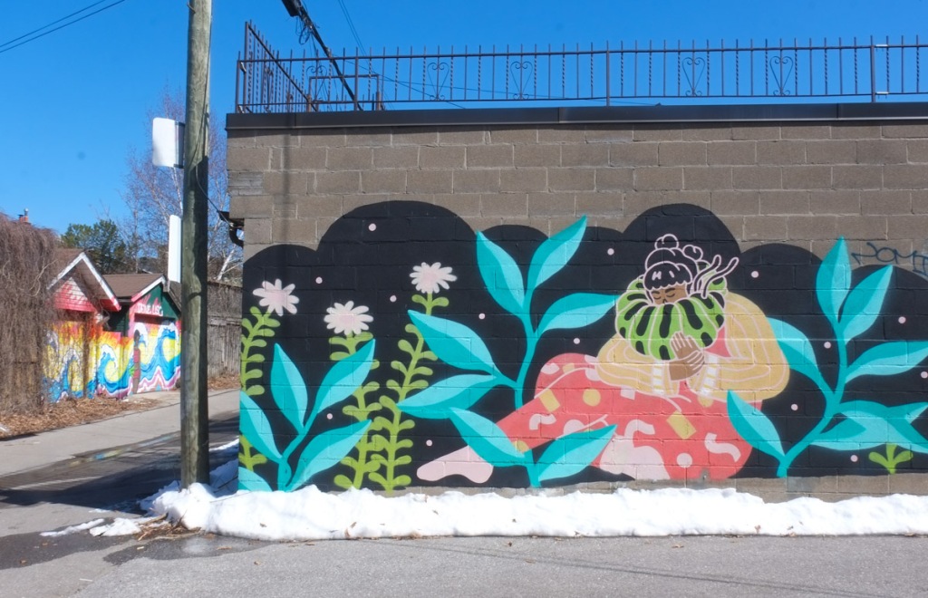 mural by Caitlin Taguibao, a woman with neck encased in green and black striped puffy thing, pupating maybe, surrounded by plants with blue leaves