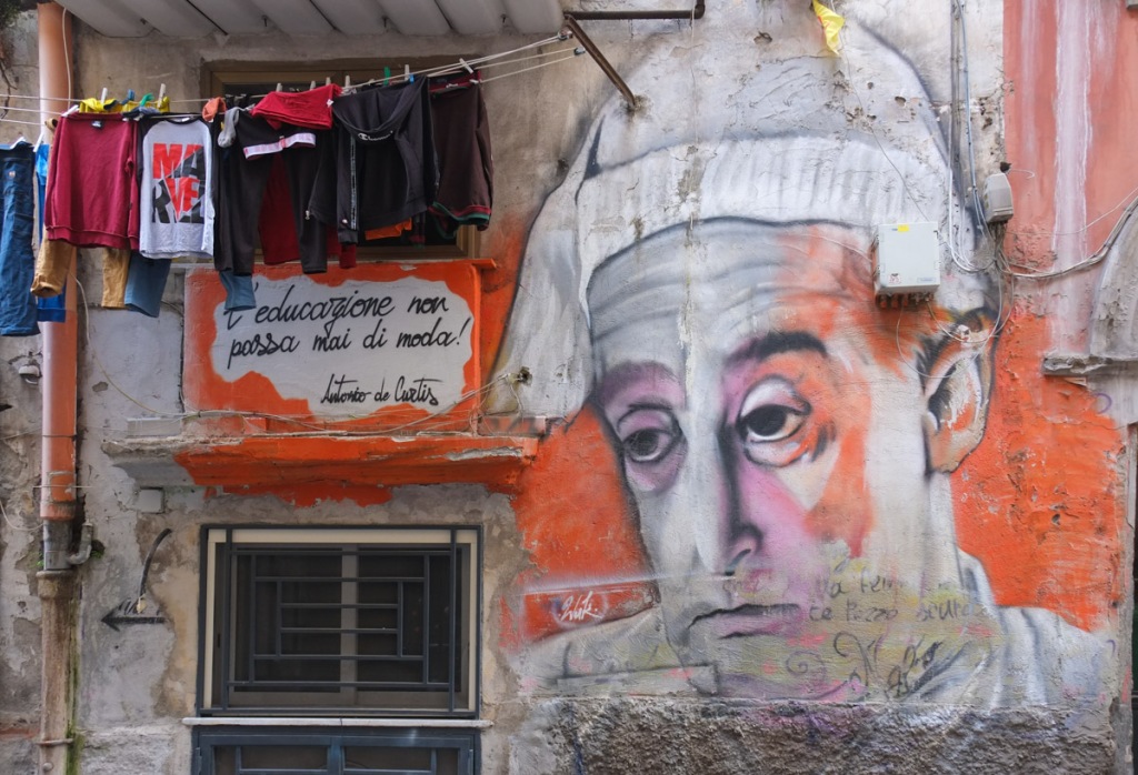 mural in Naples, man's portrait, of Toto the actor, beside a clothes line with laundry, also text in Italian that says L’educazione non passa mai di moda