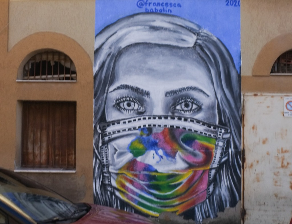 mural painted in 2020 of close up of a woman's face, wearing a brightly coloured covid mask, painted by francesca babolin