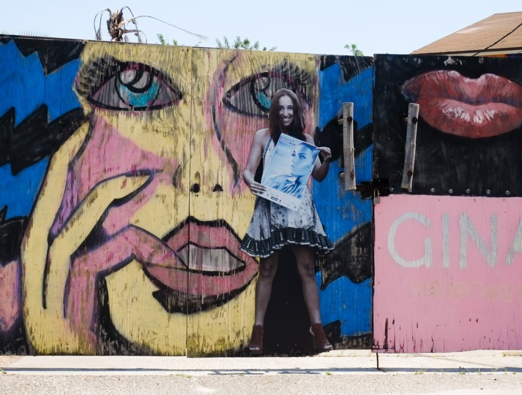 front of a low building covered with portraits and street art paintings of girls and women