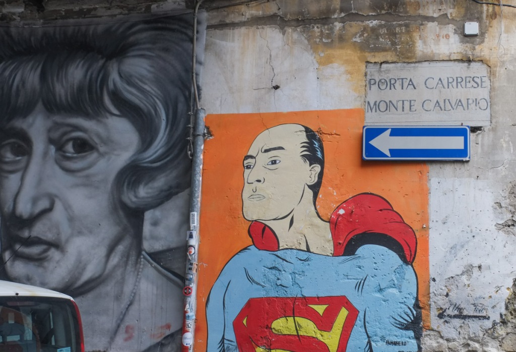 portrait of balding man in superman top and red cape, street sign for Porta Crrese Monte Calvapio, and a one way sign,