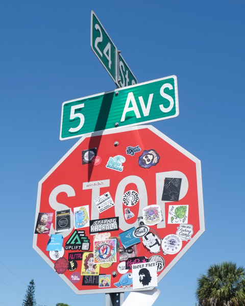 a stop sign is covered with graffiti stickers and slaps.  Also, 2 green and white St. Petersburg street signs, one for 24th Street and one for 5th Avenue South